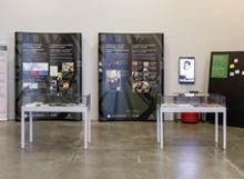 Exposition sur les Roms au Canada avec des panneaux d’information, deux expovitrines et un tableau noir avec des affiches et des notes.