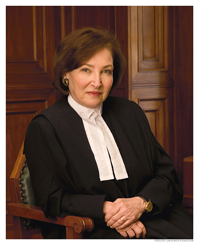 Un portrait de Rosalie Silberman Abella portant une robe de juge noire avec des onglets de col blancs, assise dans une chaise en bois.