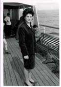 Femme en manteau sombre debout devant le banc sur le pont du navire.