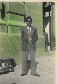 Jeune homme portant un costume et une cravate, debout sur le trottoir devant un immeuble.