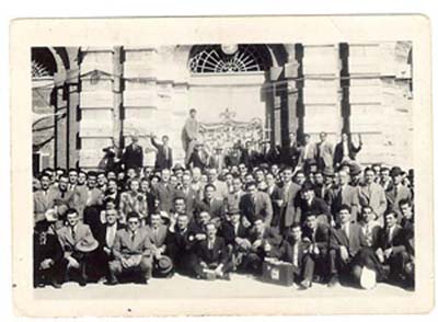 Grand groupe d’hommes assis et debout sur les marches d’un bâtiment en béton.