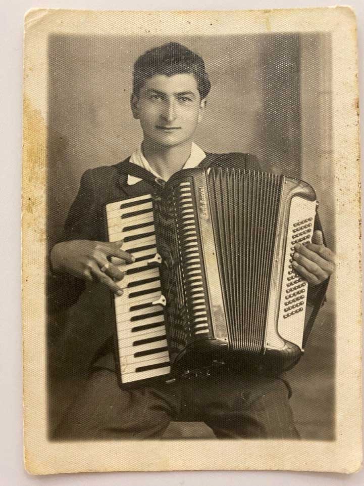 Un jeune homme sourit à l’appareil photo en jouant de l’accordéon.