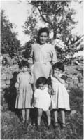 Femme avec trois enfants devant un arbre et un mur de briques. 