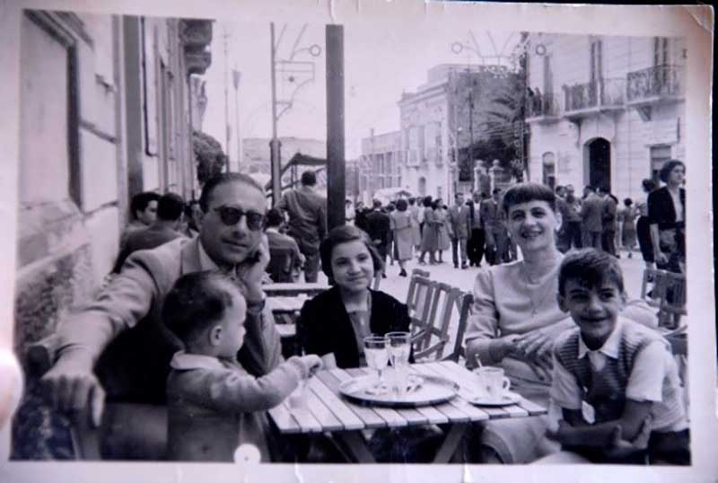 Une jeune famille s’assoit dans un café en plein air avec une pizza sur la table.