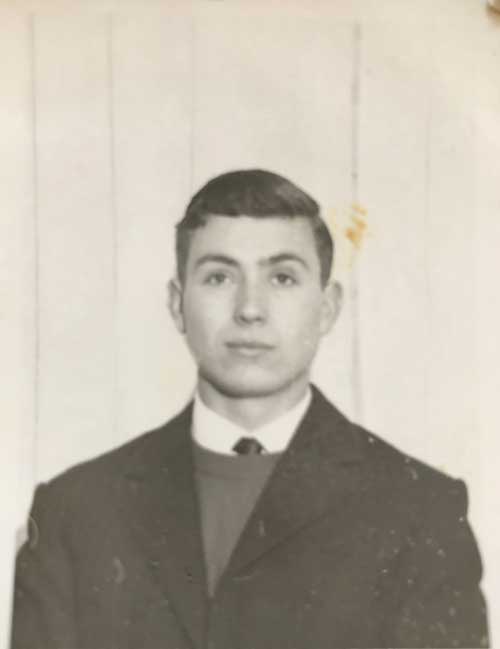 Vieille photographie fissurée sur laquelle se trouve un jeune homme portant un complet et une cravate.