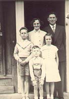Jeune homme et jeune femme avec trois enfants, debout sur les marches d’un porche.