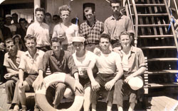 Plusieurs jeunes hommes assis ou debout derrière une bouée de sauvetage d’un bateau. 