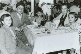 Femme assise à une table et quatre garçons d’âges variés.