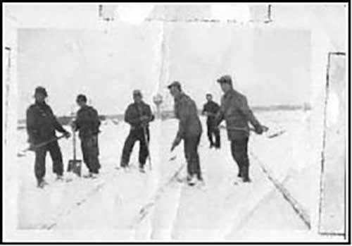Vieille photographie montrant sept hommes pelletant de la neige sur une voie de chemin de fer nouvellement construite.