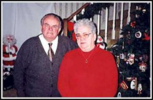 Photographie couleur d’une femme et d’un homme plus âgé devant un arbre de Noël.
