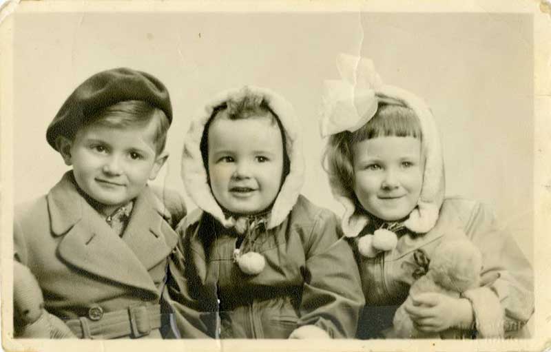 Trois petits enfants assis dans une rangée, tous portant des chapeaux d’hiver très différents.