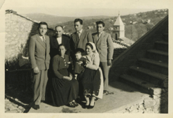 Vieille photographie à l’extérieur de deux femmes assises avec un bébé et de quatre hommes debout derrière elles.