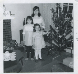 Trois jeunes filles debout près d’un arbre de Noël. 