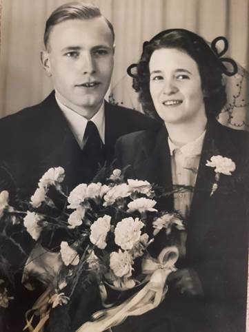 Portrait en tons sépia d’un couple hollandais blanc souriant avec des fleurs, en tenue de soirée.