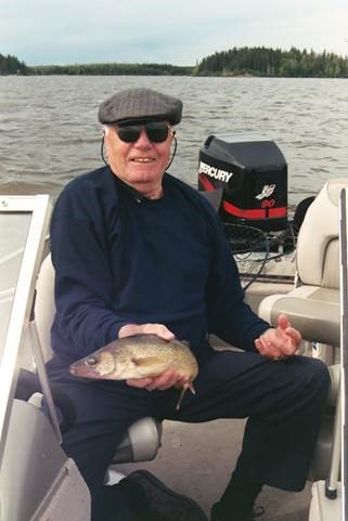 Un homme blanc d’un certain âge sur un bateau sur un lac, tenant un poisson et souriant à l’appareil photo.