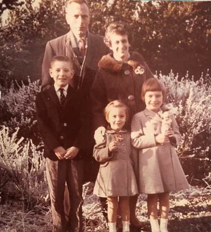 Une photo en tons sépia d’une famille blanche composée d’un homme, d’une femme et de trois enfants, tous dehors et bien habillés.