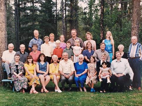 Grande photo de groupe posée d’une famille blanche, prise à l’extérieur par temps chaud, avec une forêt derrière eux.