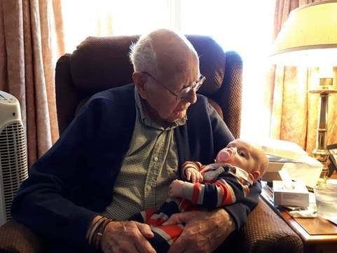 Un homme blanc âgé, assis sur une chaise et tenant un bébé dans ses bras.