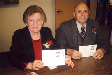 Homme et femme assis à table, portant des fleurs de rose et tenant des passeports ouverts.