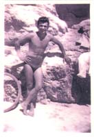 Jeune Eddy en maillot de bain, appuyé contre des rochers sur la plage.