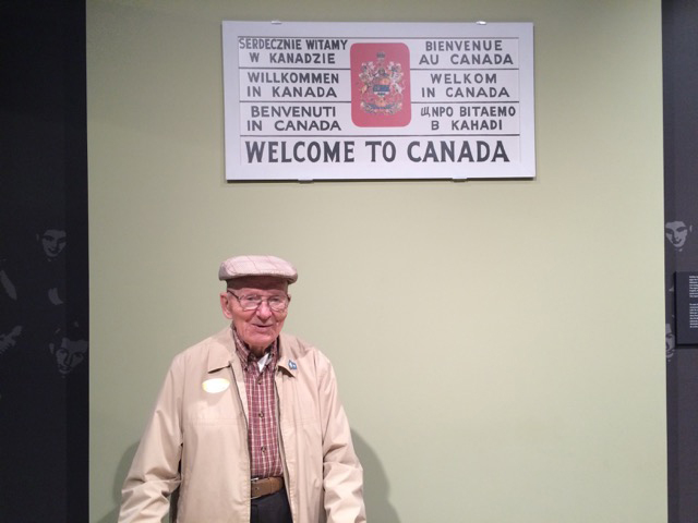 Un jeune homme se tient à côté d’une affiche qui dit Bienvenue au Canada.