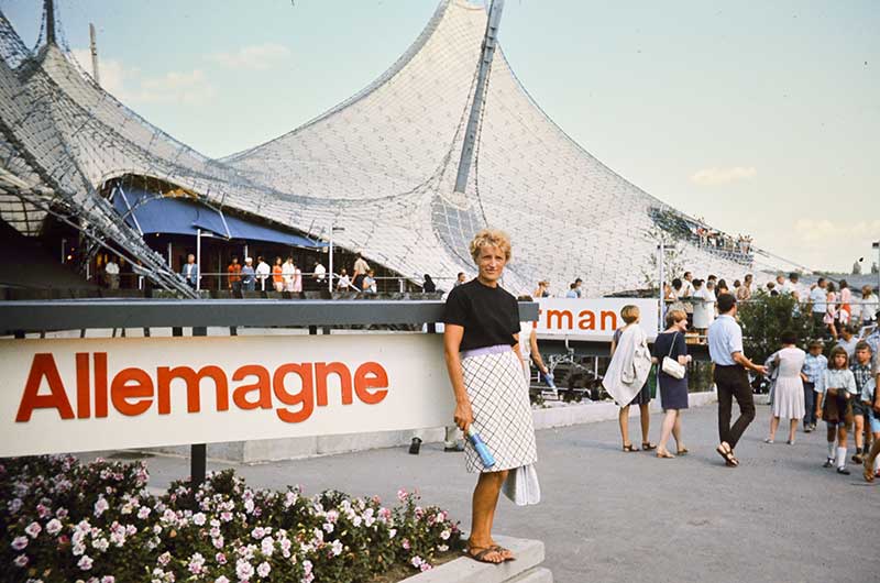 Une jeune femme devant le stade olympique de Munich. Le mot Allemagne se trouve près d’elle, écrit en grosses lettres.