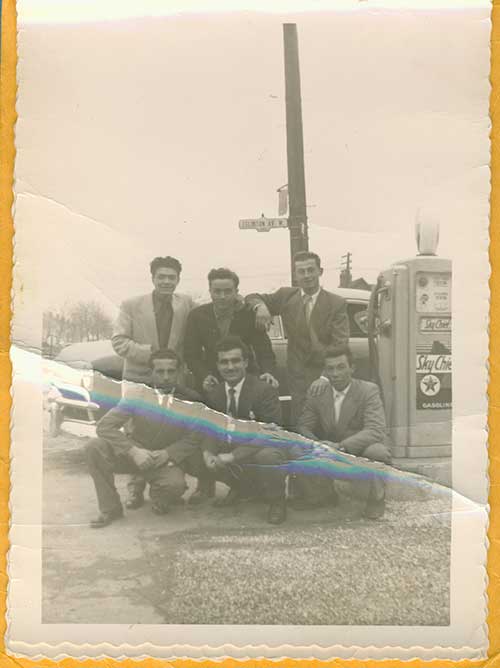 Six jeunes hommes assis à côté d’une pompe à essence.