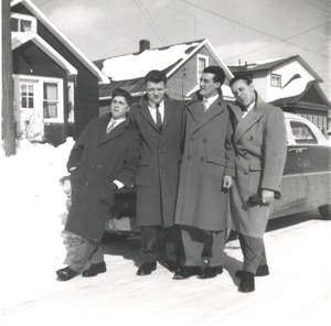 Quatre jeunes hommes en pardessus sur une rue enneigée.