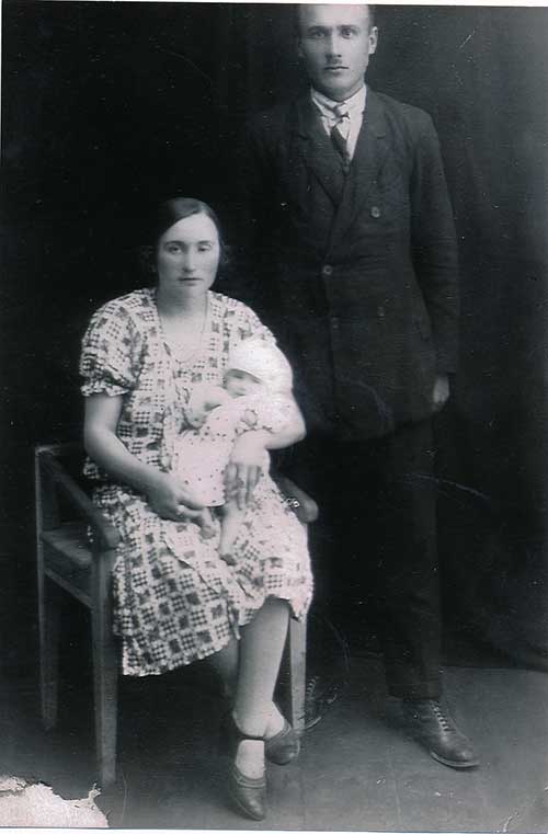 Image d’archives d’une femme assise avec un bébé dans ses bras, un homme en noir se tient à côté d’elle.