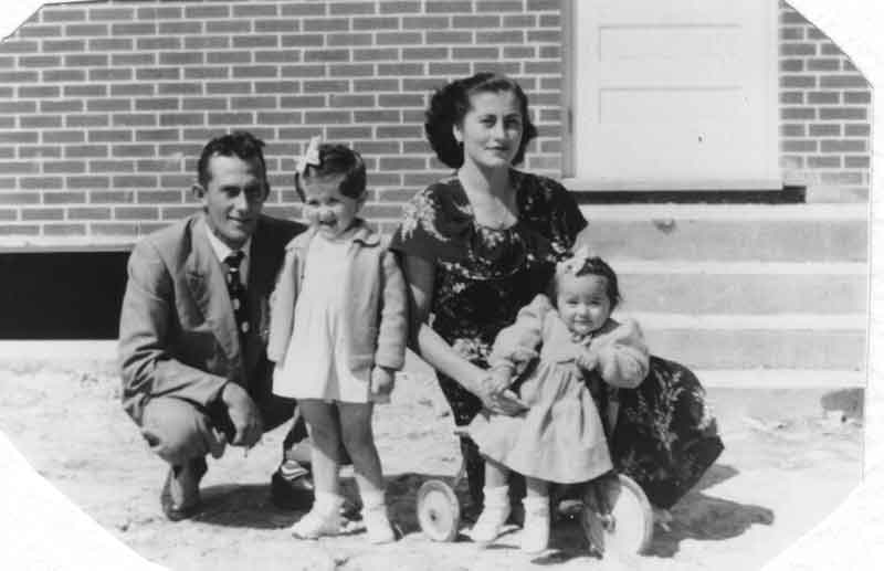 Photo en noir et blanc d’un jeune couple avec deux enfants devant leur maison.