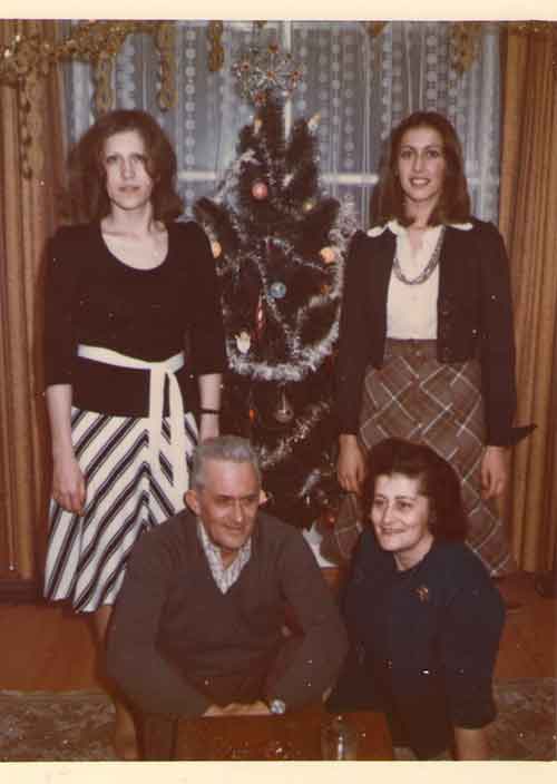 Deux jeunes femmes debout de chaque côté d’un arbre de Noël et un couple assis devant.