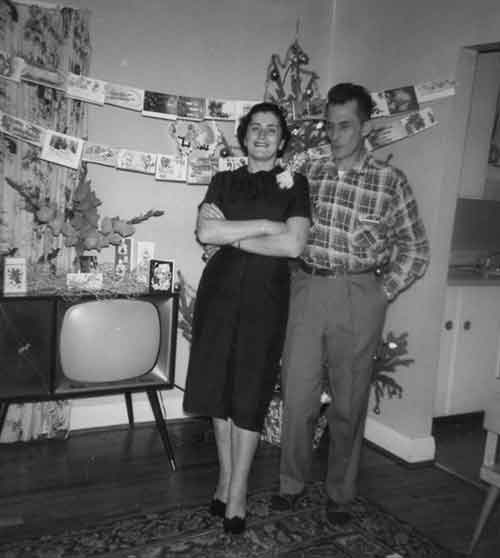Couple est debout à côté de l’autre avec des cartes de vœux sur le mur arrière et sur le dessus de la télévision.