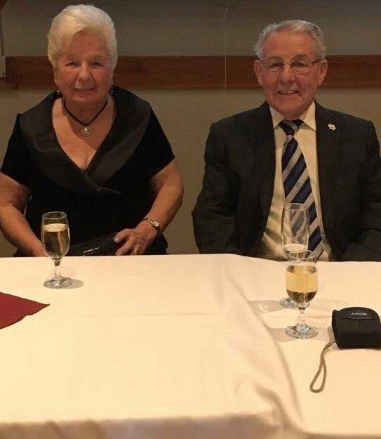 Un couple âgé assis à une table de banquet. Ils boivent du vin blanc.