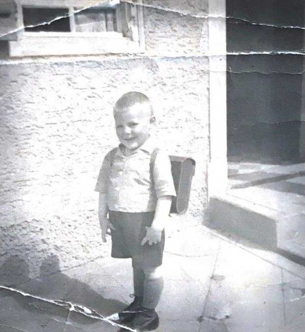 Vieille photographie fissurée sur laquelle se trouve un petit garçon souriant portant un sac à dos.