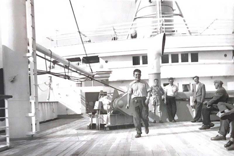 De jeunes hommes sur le pont d’un navire. L’un d’entre eux marche en direction de l’appareil photo.