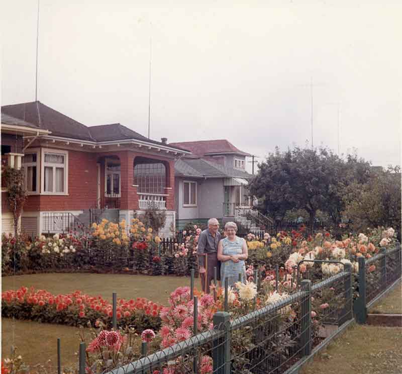 Un homme et une femme au fond de leur jardin rempli de belles fleurs.