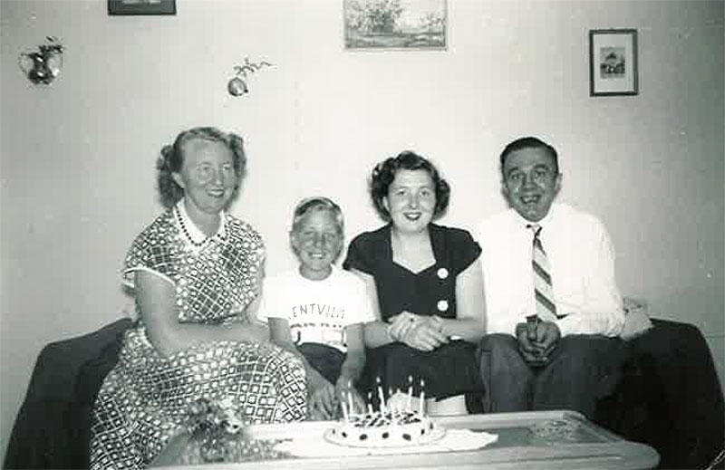 Une jeune famille est assise sur un canapé avec un gâteau sur la table devant eux.