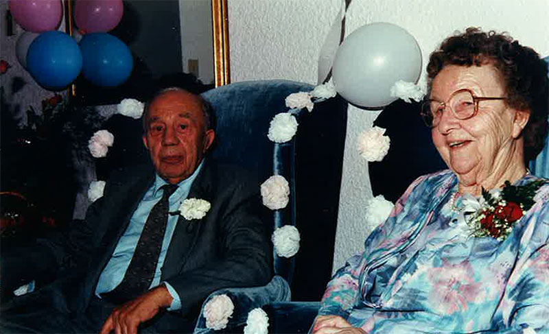 Un jeune couple est assis sur des chaises ailées décorées de fleurs blanches et de ballons.