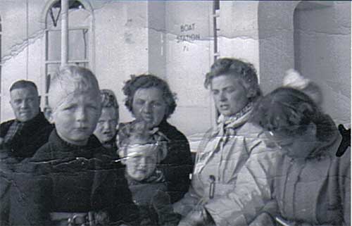 Photo en noir et blanc de trois femmes, un homme et trois enfants, ils sont assis sur un bateau.