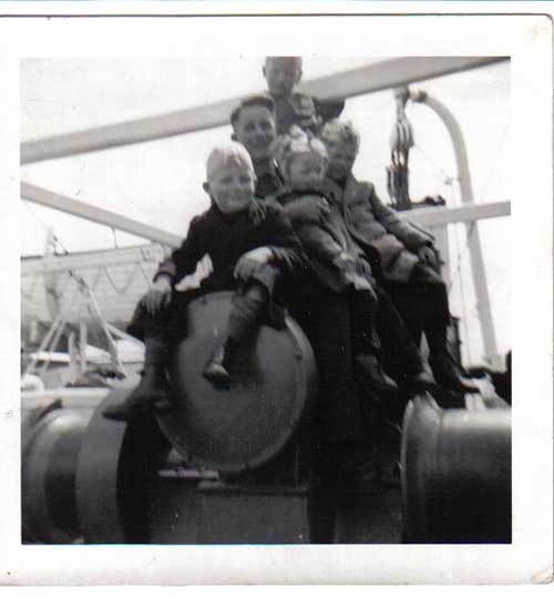 Quatre enfants avec un homme assis sur le pont du navire.