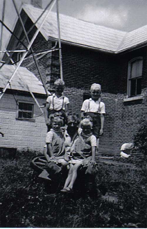Un homme avec quatre enfants assis sur l’herbe devant une maison.