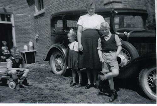Deux enfants et une femme se tiennent devant une voiture. 