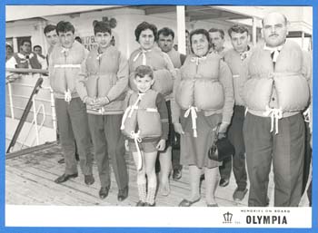 Hommes, femmes et enfants debout sur le pont du navire portant des gilets de sauvetage.