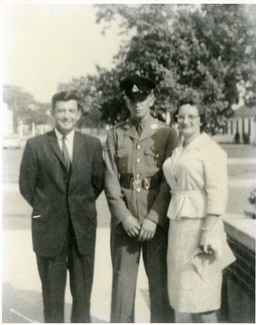Homme et femme debout avec un jeune homme en uniforme militaire, un arbre peut être vu dans le fond.