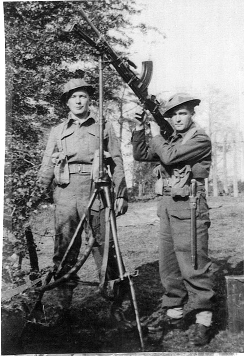 Deux jeunes hommes en uniforme militaire tiennent des armes et posent pour la caméra.