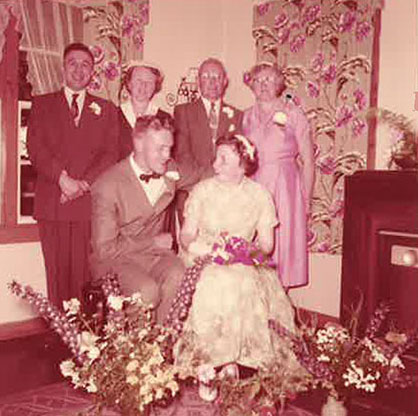 Un couple nouvellement marié est assis et quatre invités se tiennent derrière eux.
