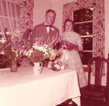 Un couple nouvellement marié se tient derrière une table chargée de nourriture et de boisson.