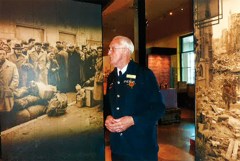Un homme en uniforme de guide touristique se tient devant une exposition de musée.