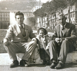 Deux hommes assis sur des blocs de pierre dans la place de la ville avec un petit enfant entre eux.