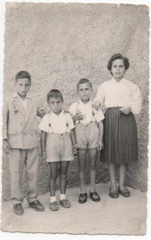 Vieille photo en noir et blanc de trois enfants debout avec une jeune femme devant le mur pour la photo.